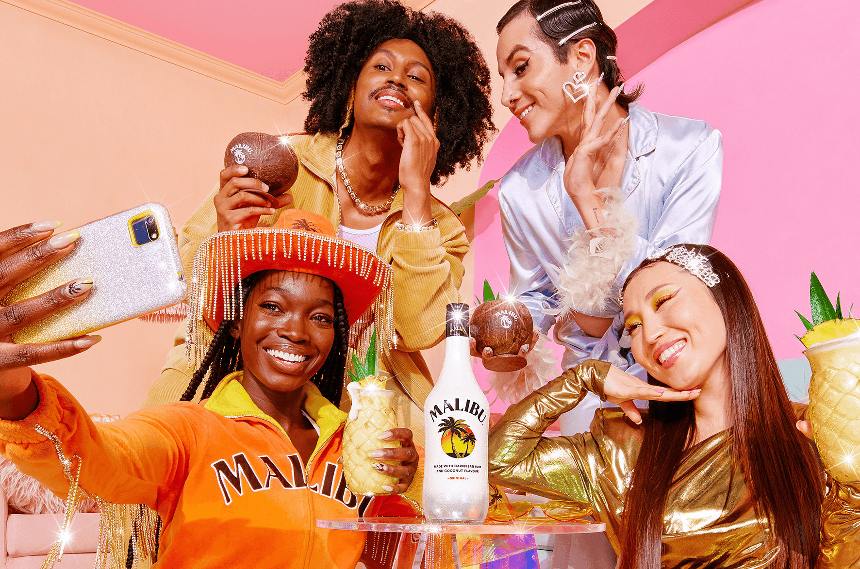 Vier Personen posieren bei einer farbenfrohen Party mit Malibu-Flasche und tropischen Drinks für ein gemeinsames Selfie.
